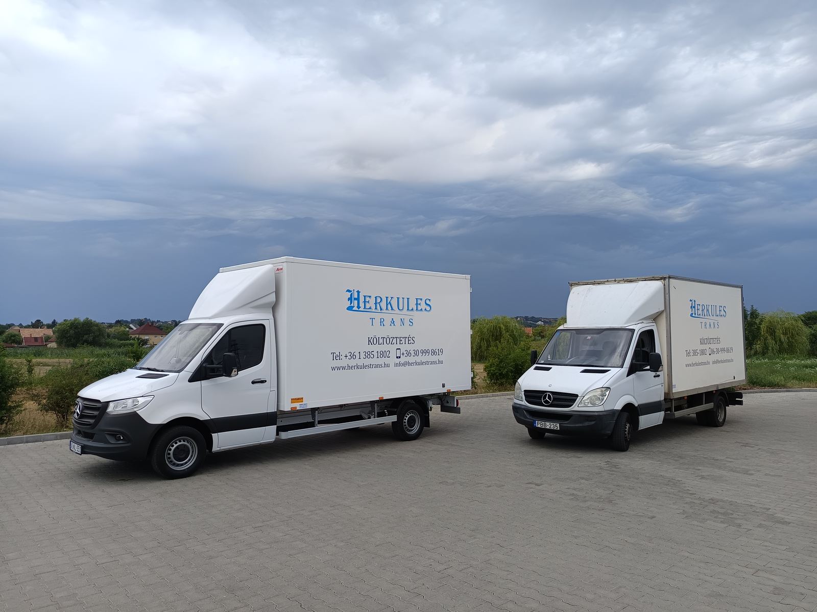 Two Herkules-Trans trucks in a paved car park Two Herkules-Trans moving trucks in a paved car park under a stormy sky